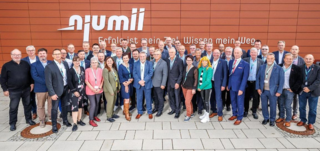 Das Bild zeigt eine große Gruppe von Menschen vor einem modernen Gebäude mit dem Schriftzug "n'umi". Alle scheinen freundlich und erfreut.